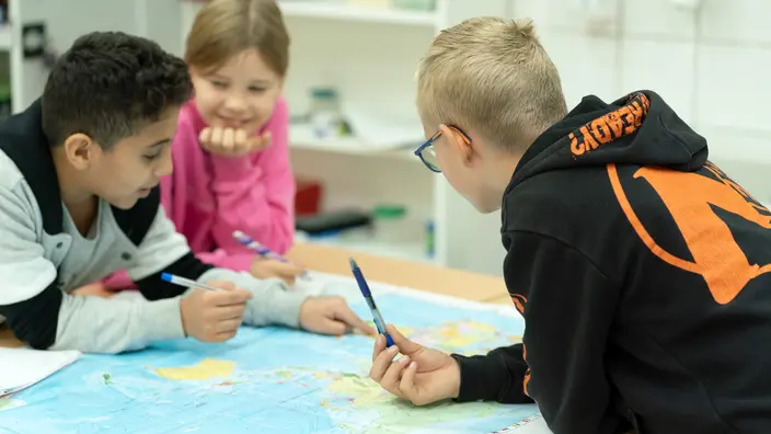 Mehrere Schüler lehnen über einer Weltkarte