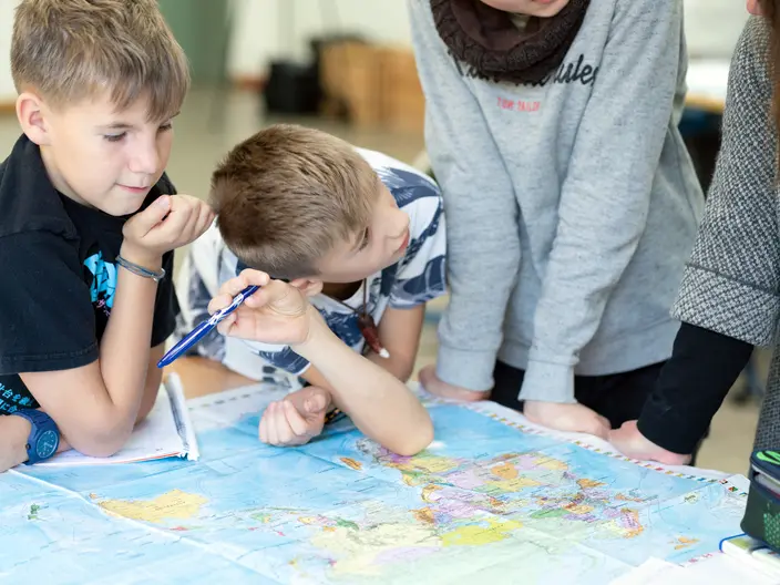 Mehrere Schüler lehnen über einer Weltkarte.